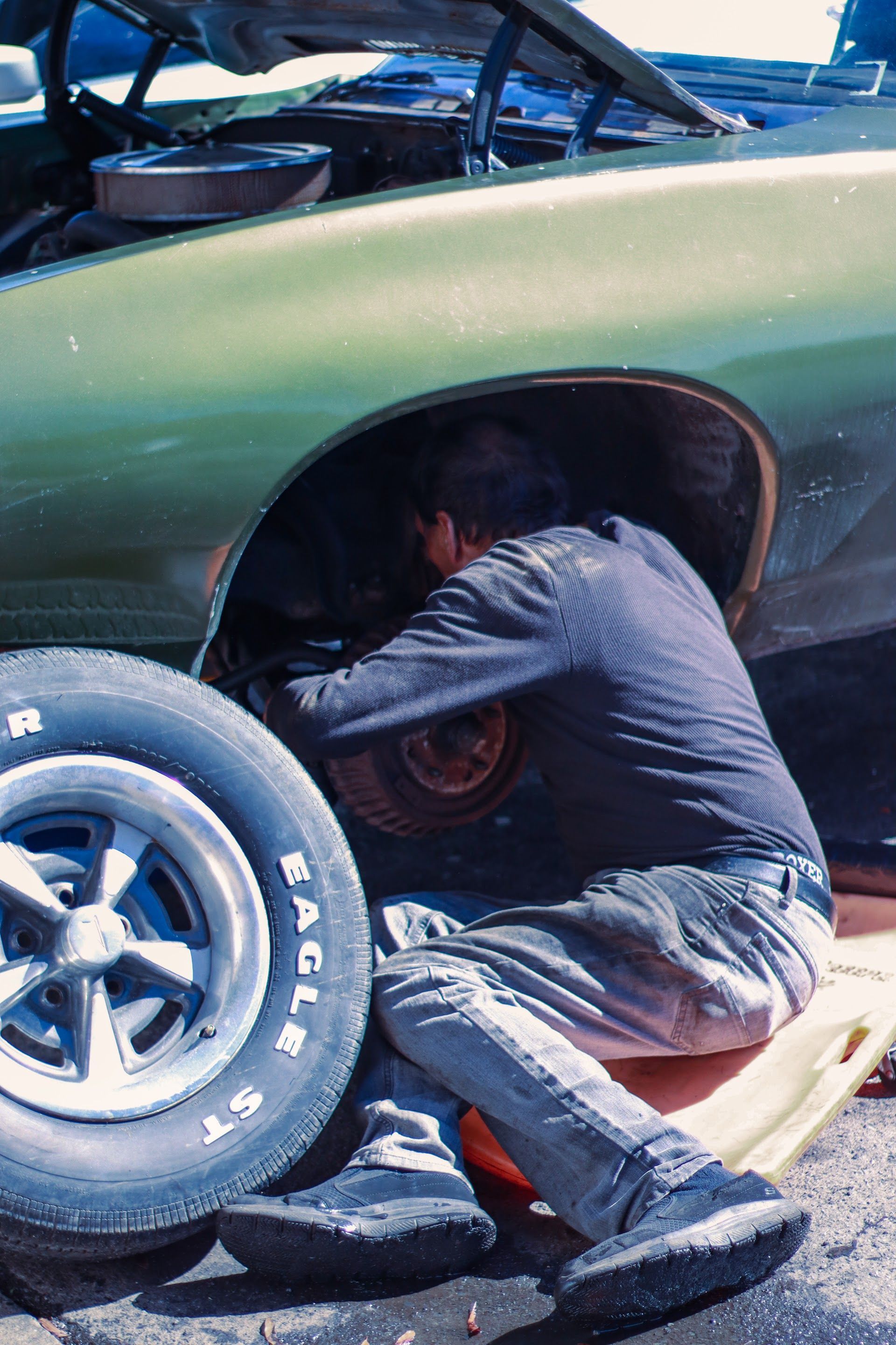 Person working on a car, crouched near a tire, under the wheel well, outdoors | Lowry Auto Service