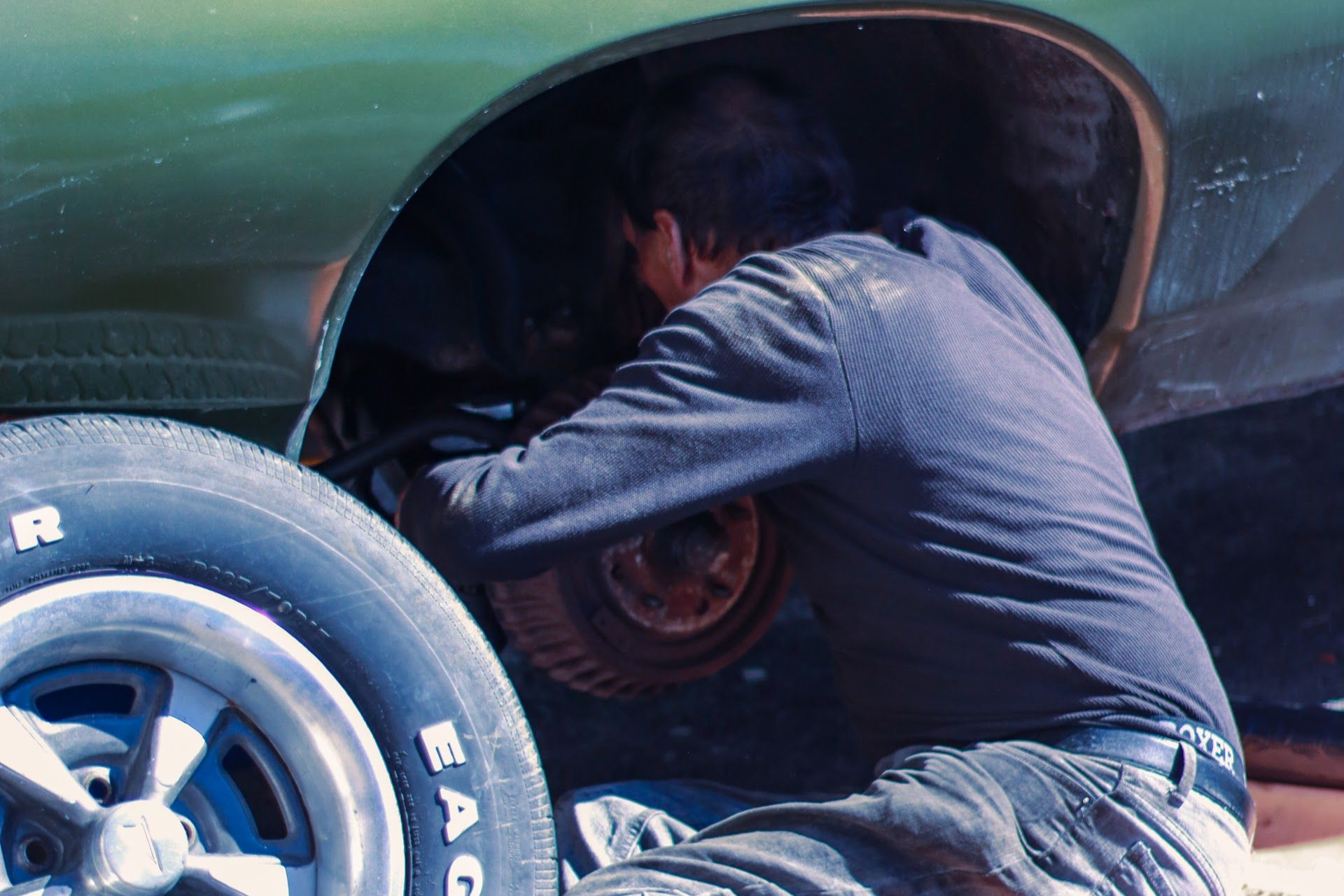 Person working on a car's wheel, likely repairing or replacing parts. The car is green | Lowry Auto Service