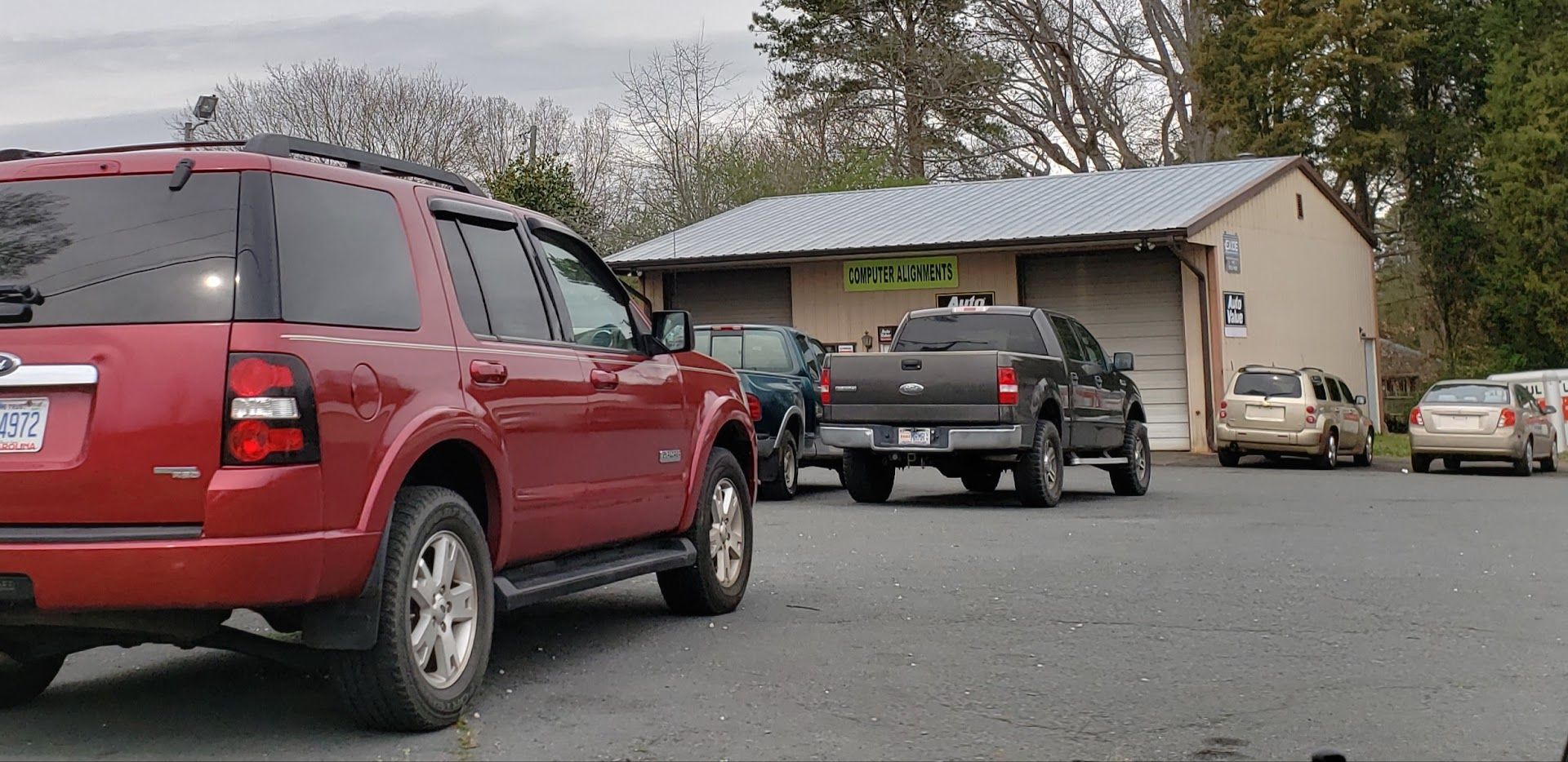 Red SUV parked, with a pickup truck and other vehicles parked near a small building | Lowry Auto Service