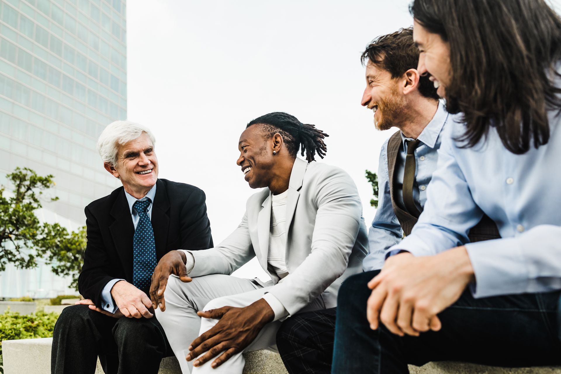 A group of men are sitting on a bench talking to each other.