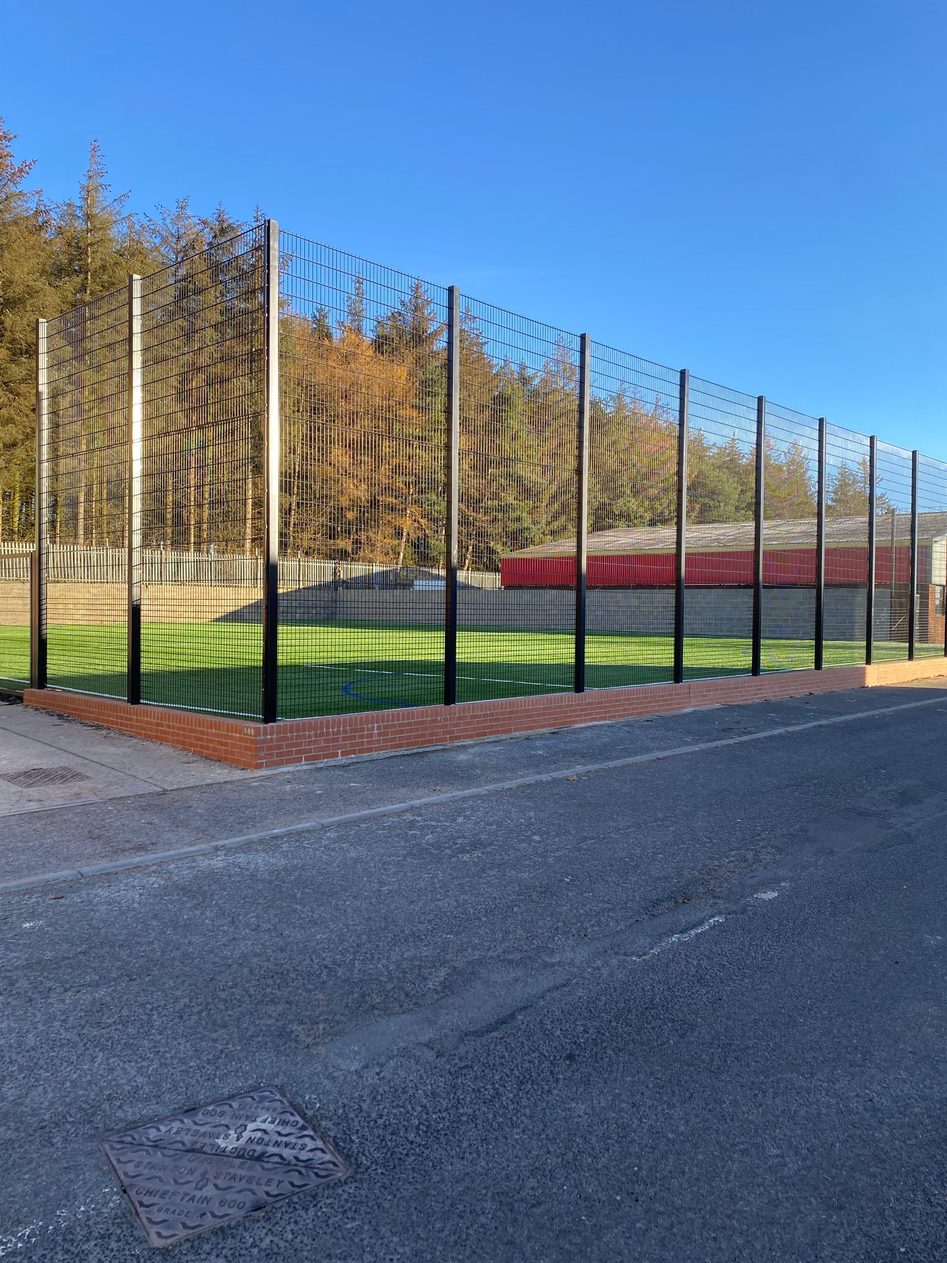 Black metal fence encloses a green lawn with a red building in the background, blue sky.