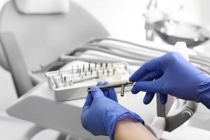 In un ambiente clinico sterile, un dentista con guanti blu tiene in mano uno strumento chirurgico metallico sopra un vassoio di strumenti.