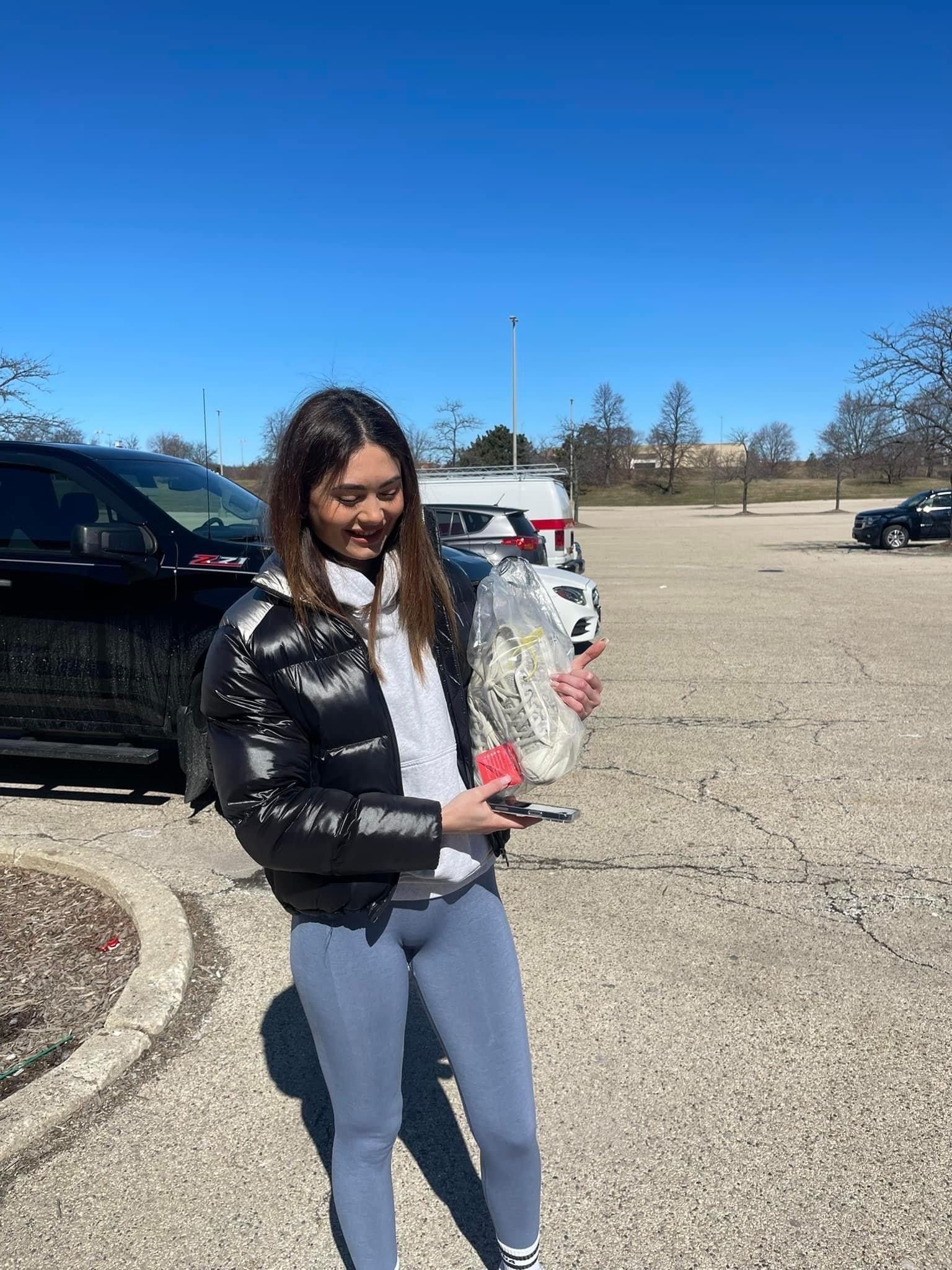 A woman is standing in a parking lot holding a bag of food.