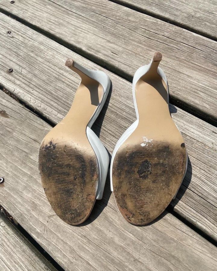 A pair of white high heels are sitting on a wooden deck.