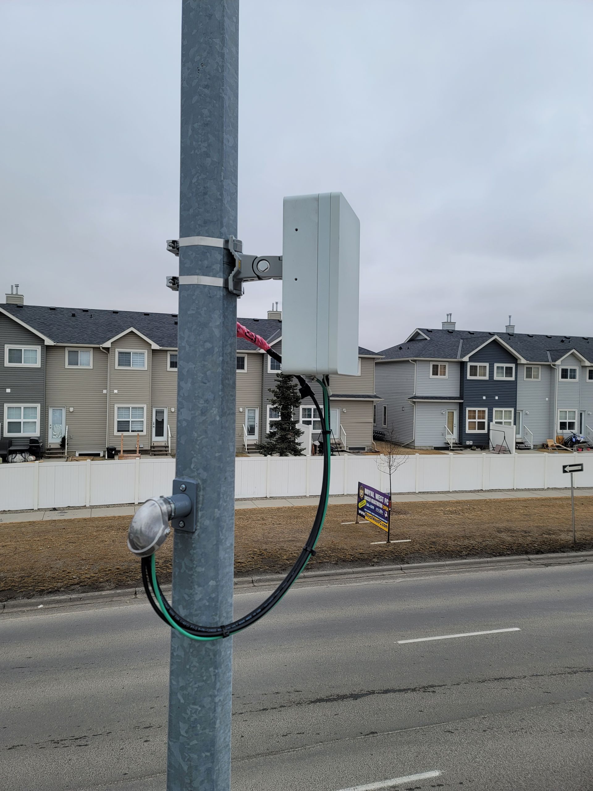 A pole with a box attached to it is on the side of the road.