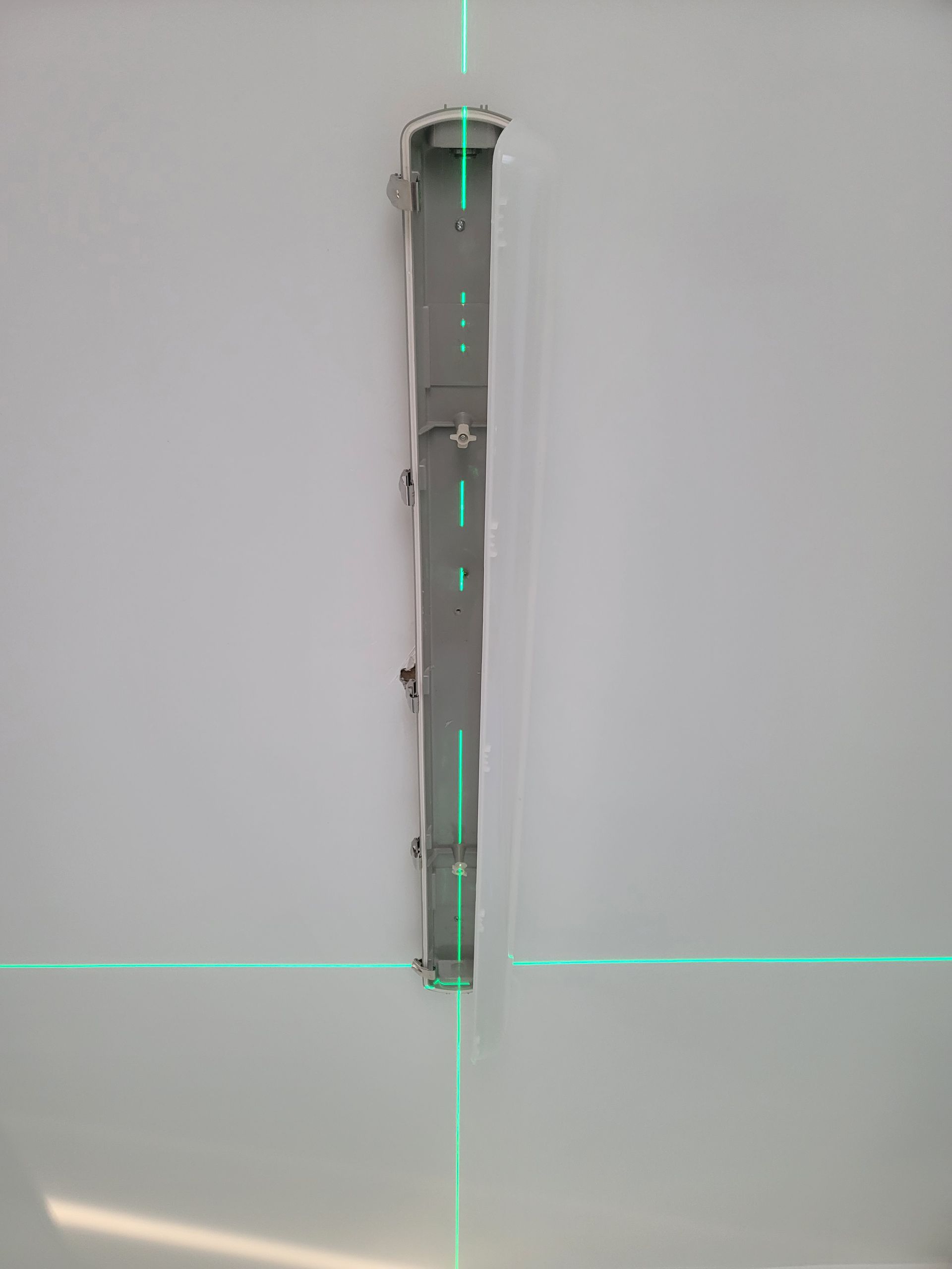 A green laser is being used to measure a piece of metal on a wall.