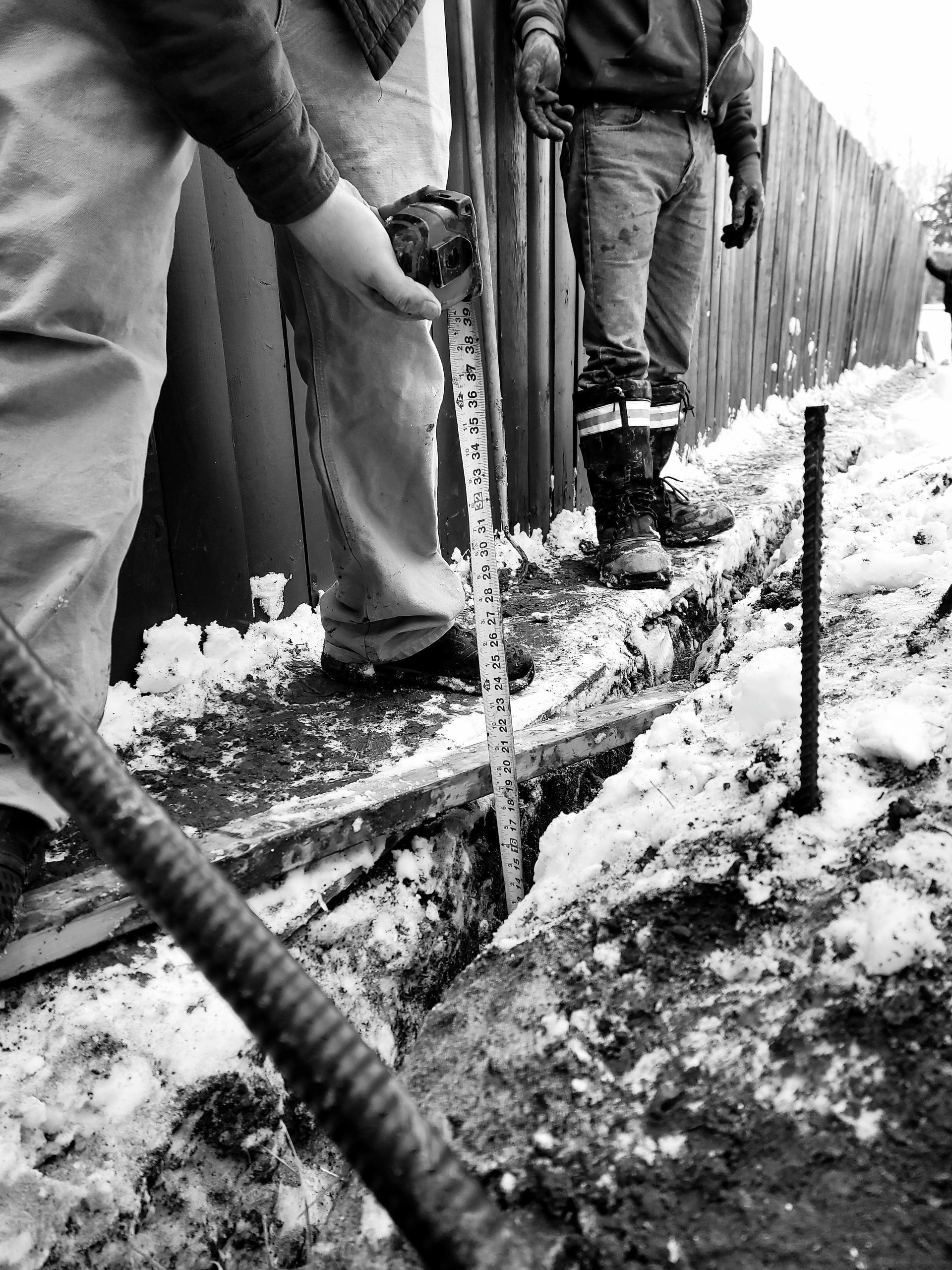 A black and white photo of a man measuring a hole with a tape measure