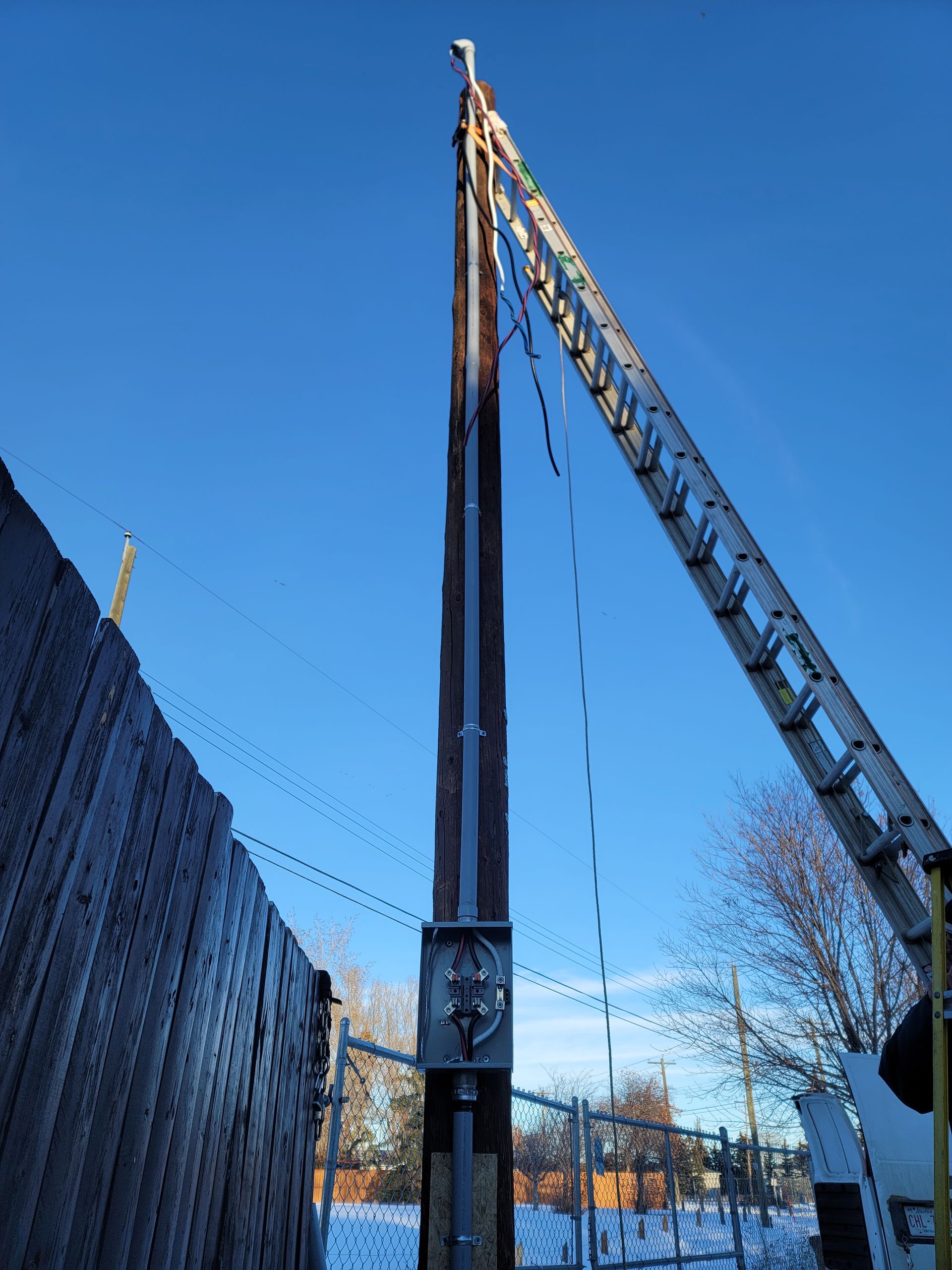 A crane with a ladder attached to it is working on a pole