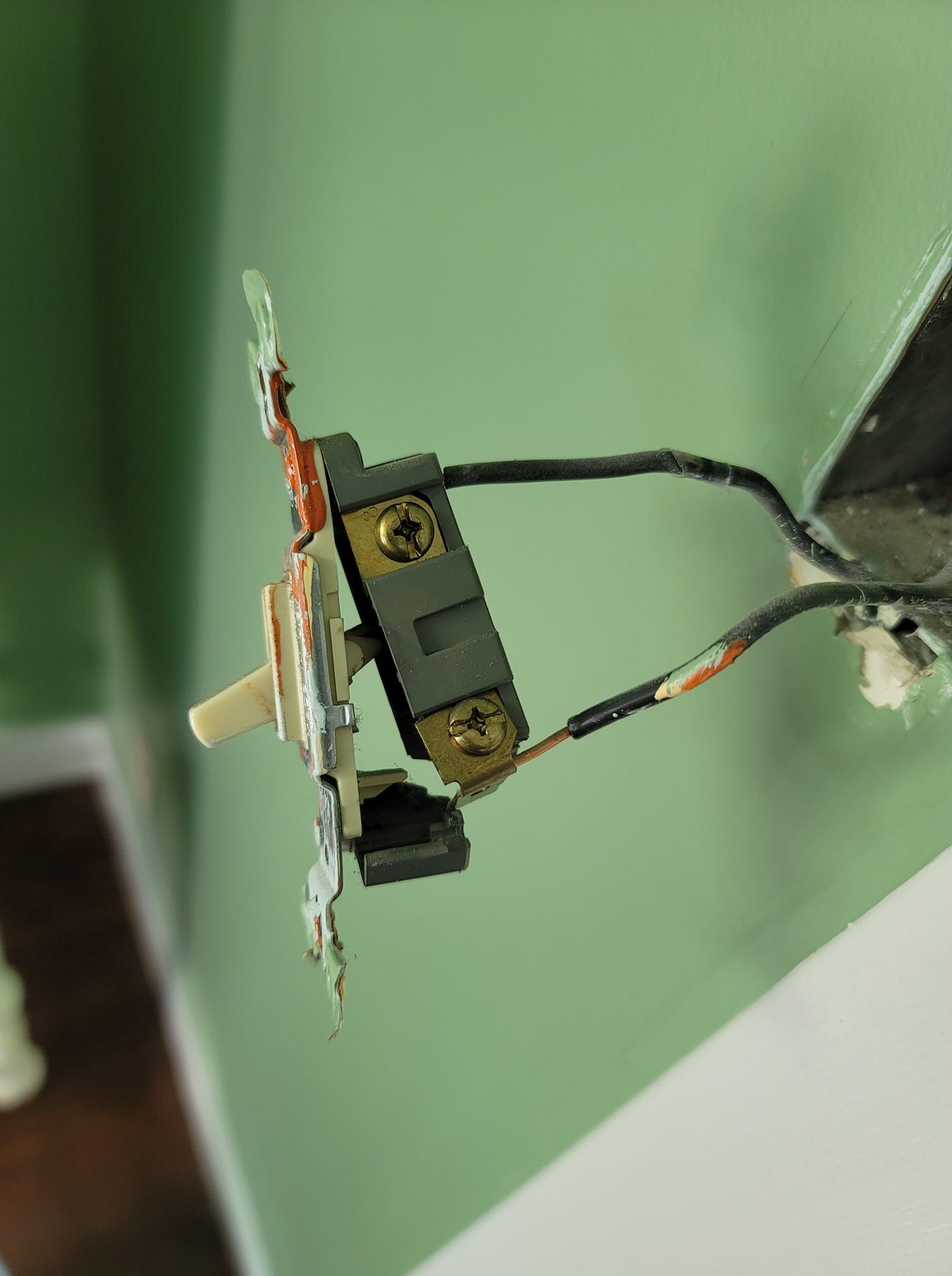 Light switch with connected wires, mounted on a green wall.