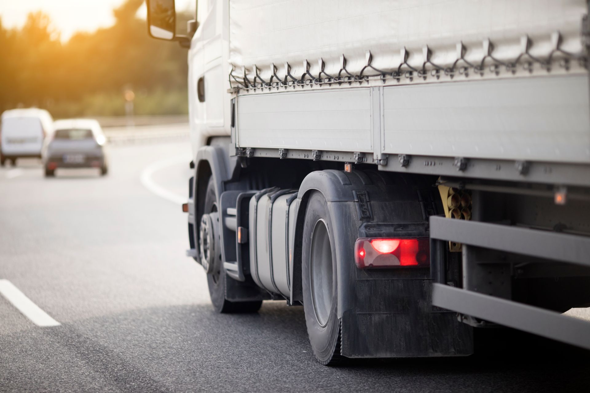 Rear view of a cargo truck driving on a highway at sunset.