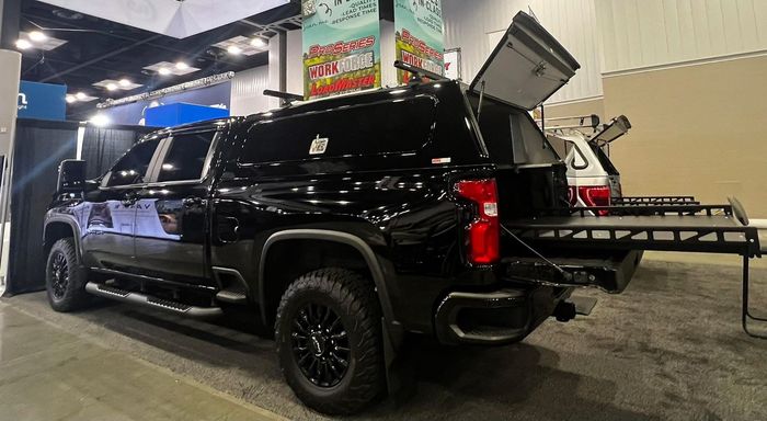 Black pickup truck with camper shell, open rear, and extending cargo platform at a convention.