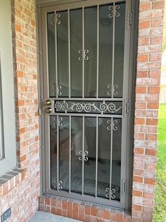 Brown metal security door with decorative scrollwork, in a brick doorway.