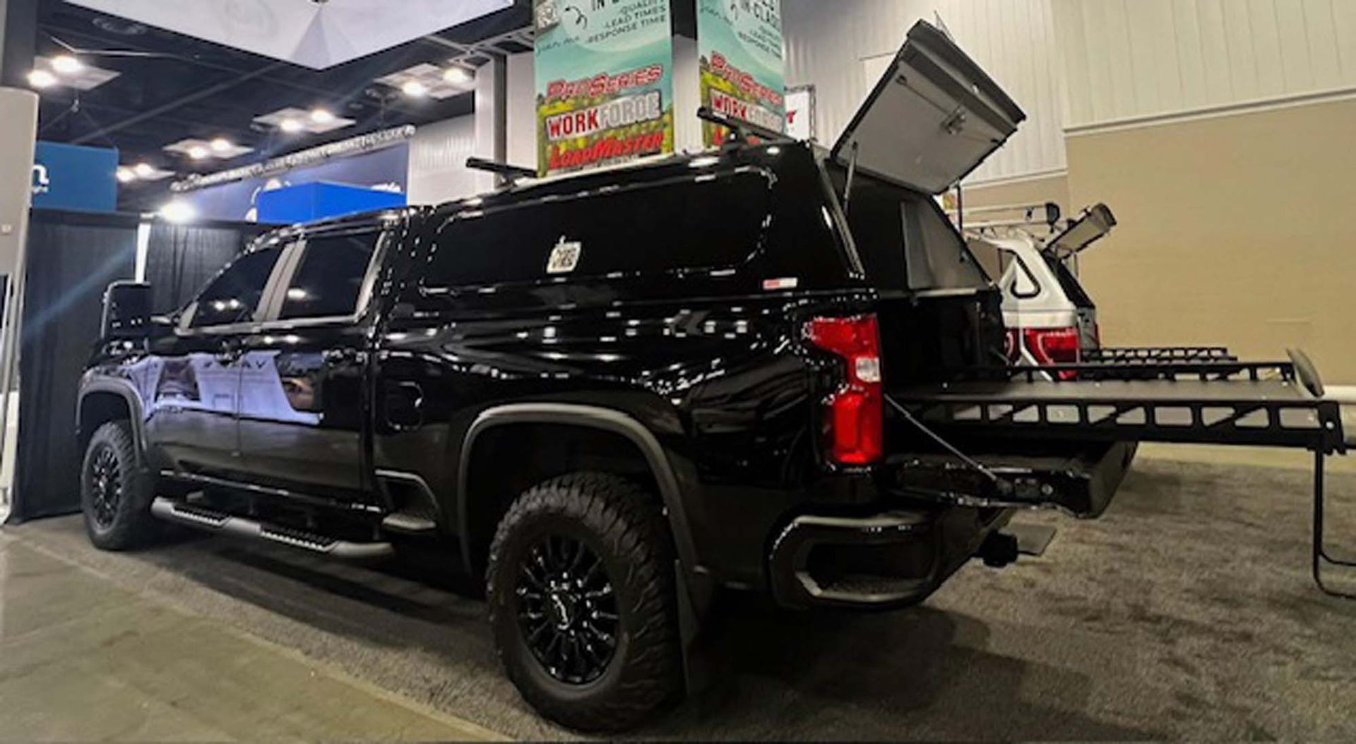 Black pickup truck with a camper shell and a pull-out bed, displayed at an indoor event.