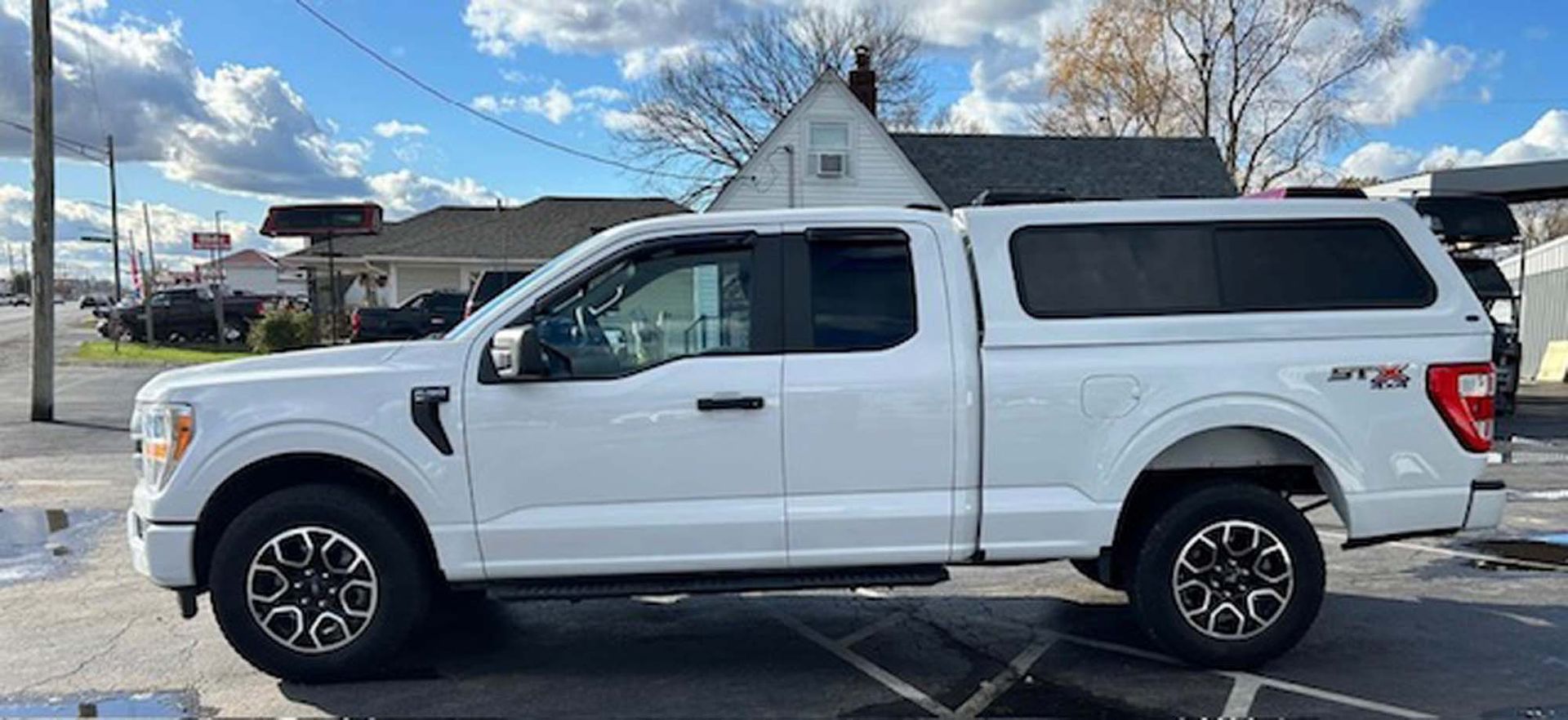 White Ford F-150 pickup truck with a cap parked on a street on a sunny day.