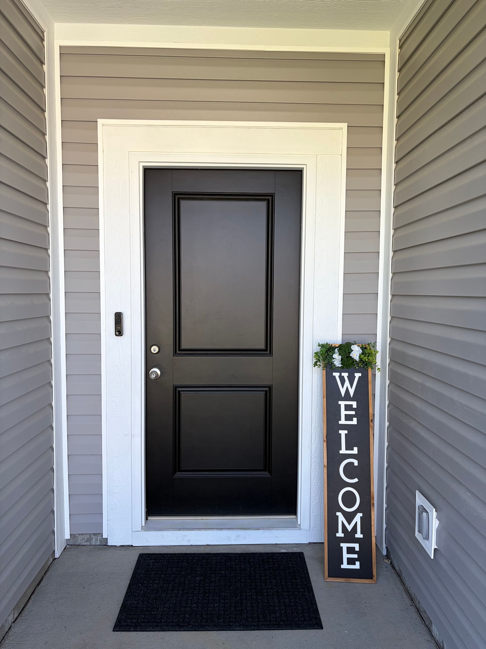 Black front door with a welcome sign on a gray house porch.