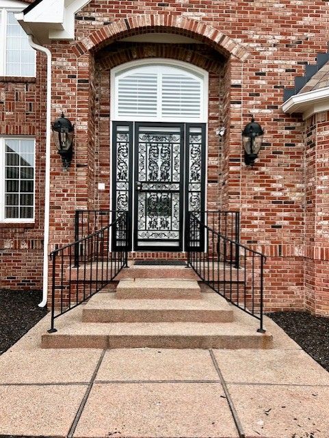 A brick house with a wrought iron door and steps leading to it.
