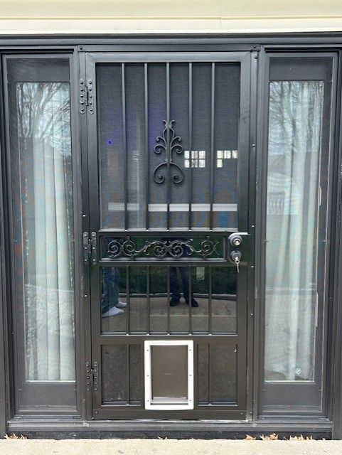 Black security screen door with a small pet door, between glass side panels.