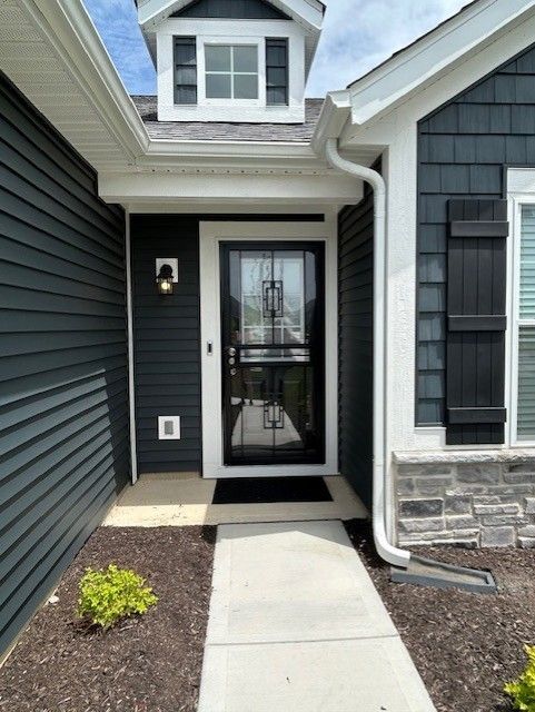 Dark blue house entrance with black door and shutters, pathway, and small landscaping.