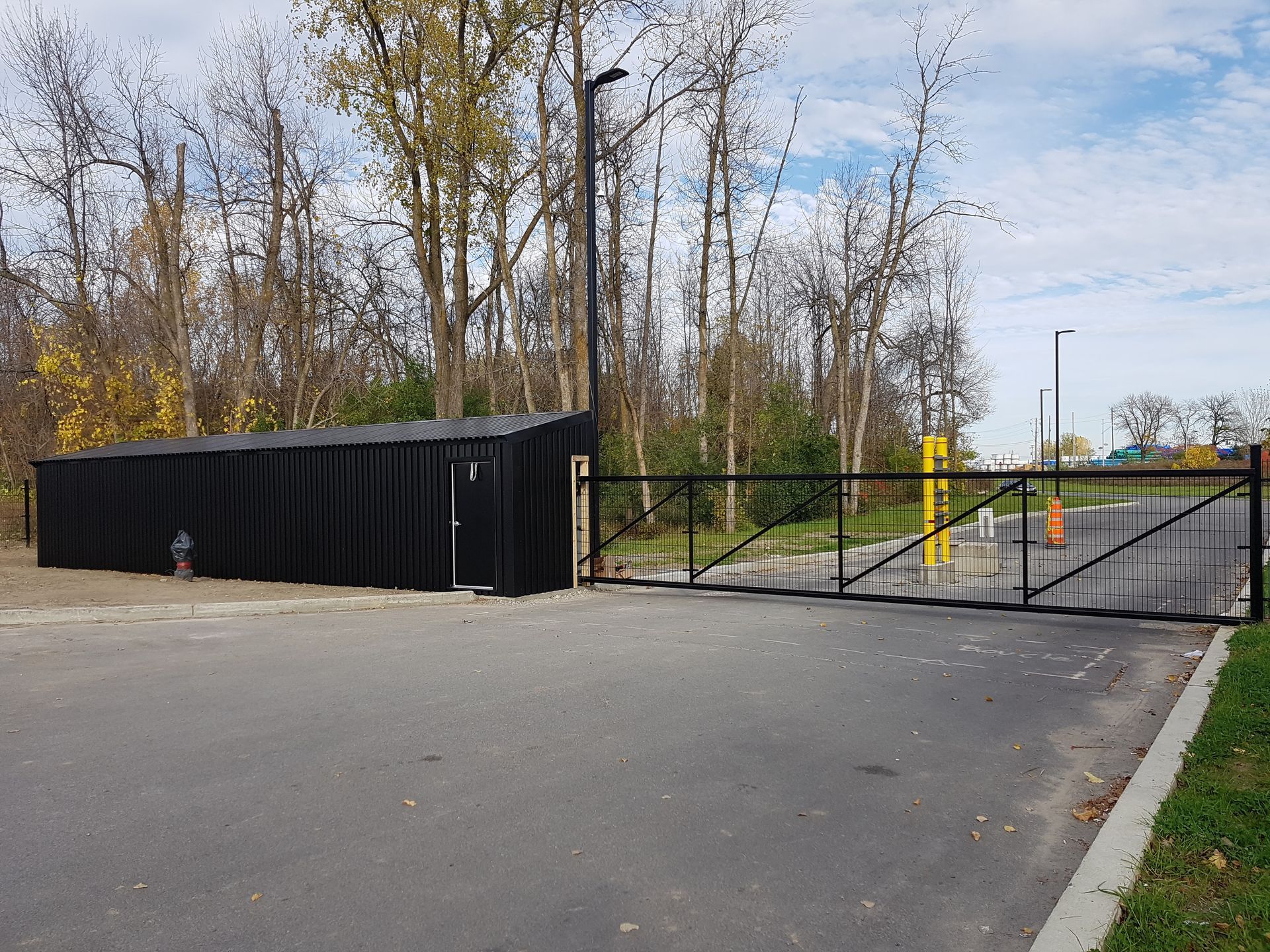 Un bâtiment noir se trouve derrière une porte métallique sur le côté d'une route.