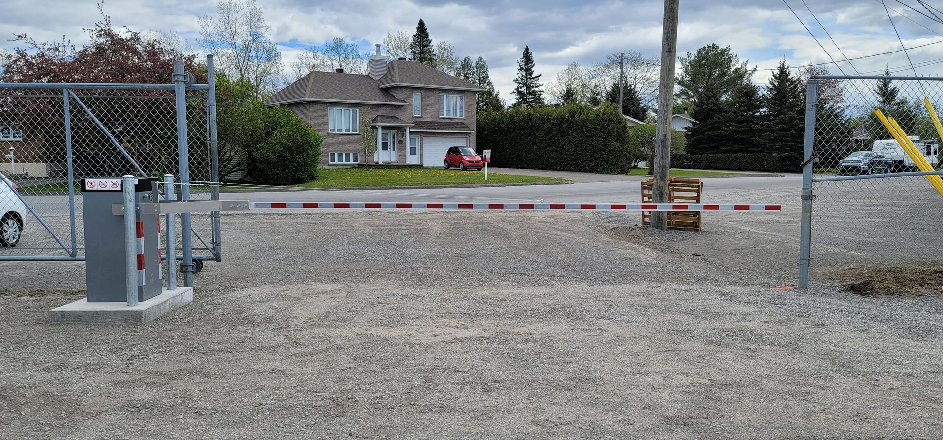 Un parking avec un portail et une maison en arrière-plan.
