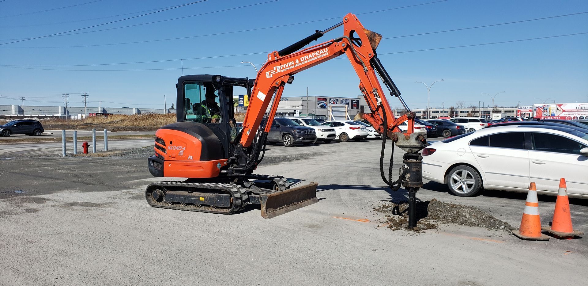 Une petite excavatrice orange creuse un trou dans un parking.