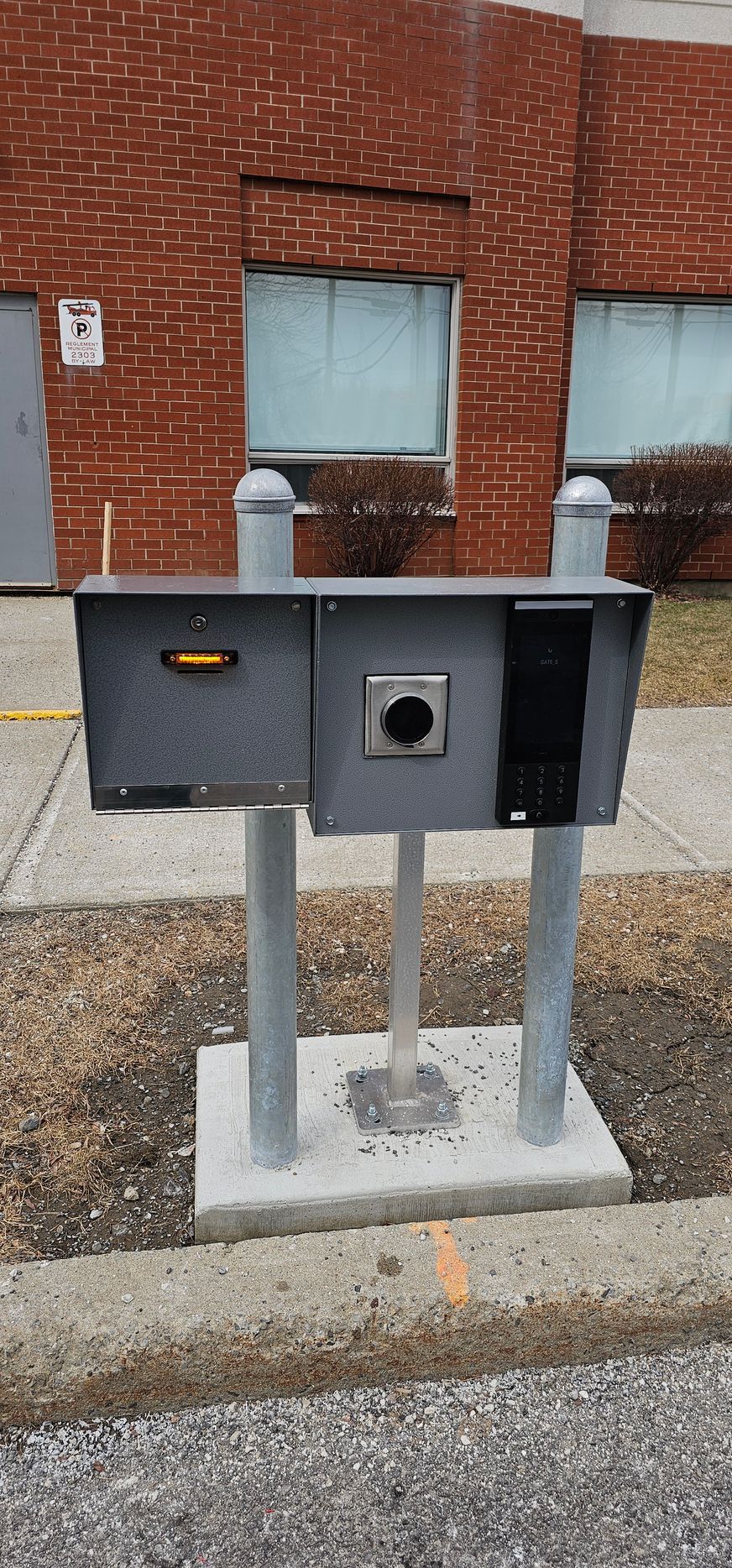 Une boîte aux lettres se trouve sur le bord de la route devant un bâtiment en briques.