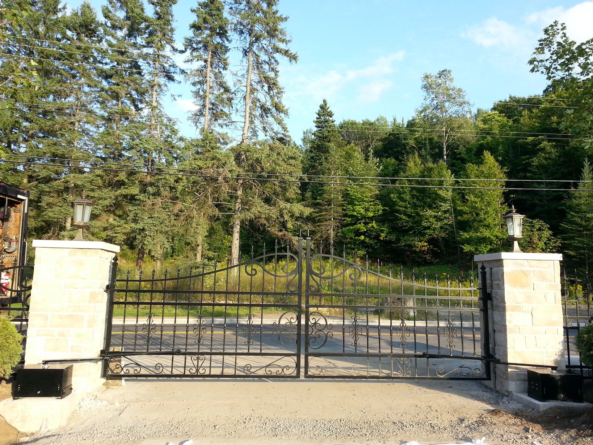 Un portail en fer forgé s'ouvre sur une allée avec des arbres en arrière-plan