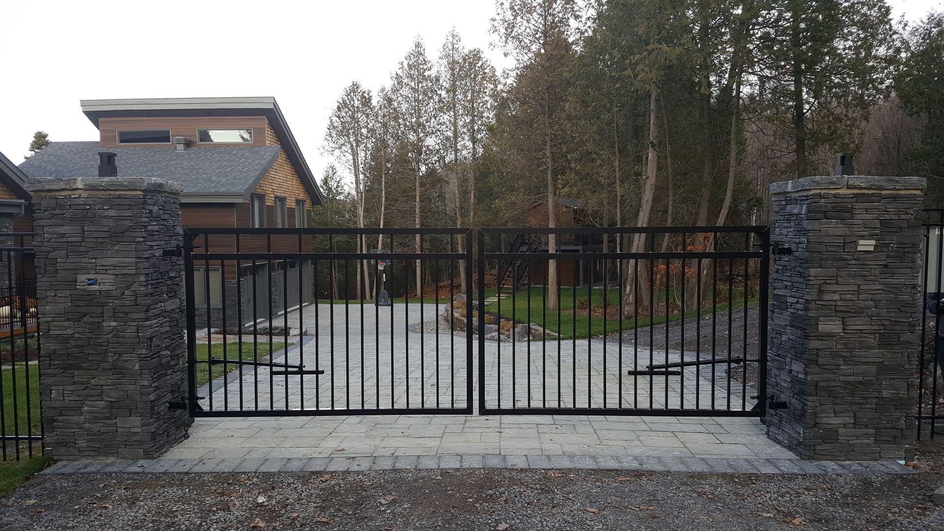 Un portail noir est ouvert sur une allée devant une maison.