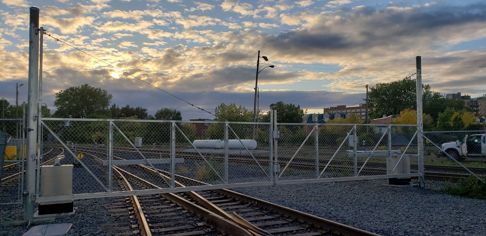 Une voie ferrée avec une clôture et un coucher de soleil en arrière-plan.