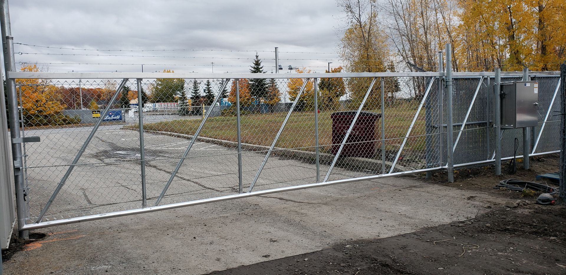 Une clôture à mailles losangées est posée sur une route de gravier.