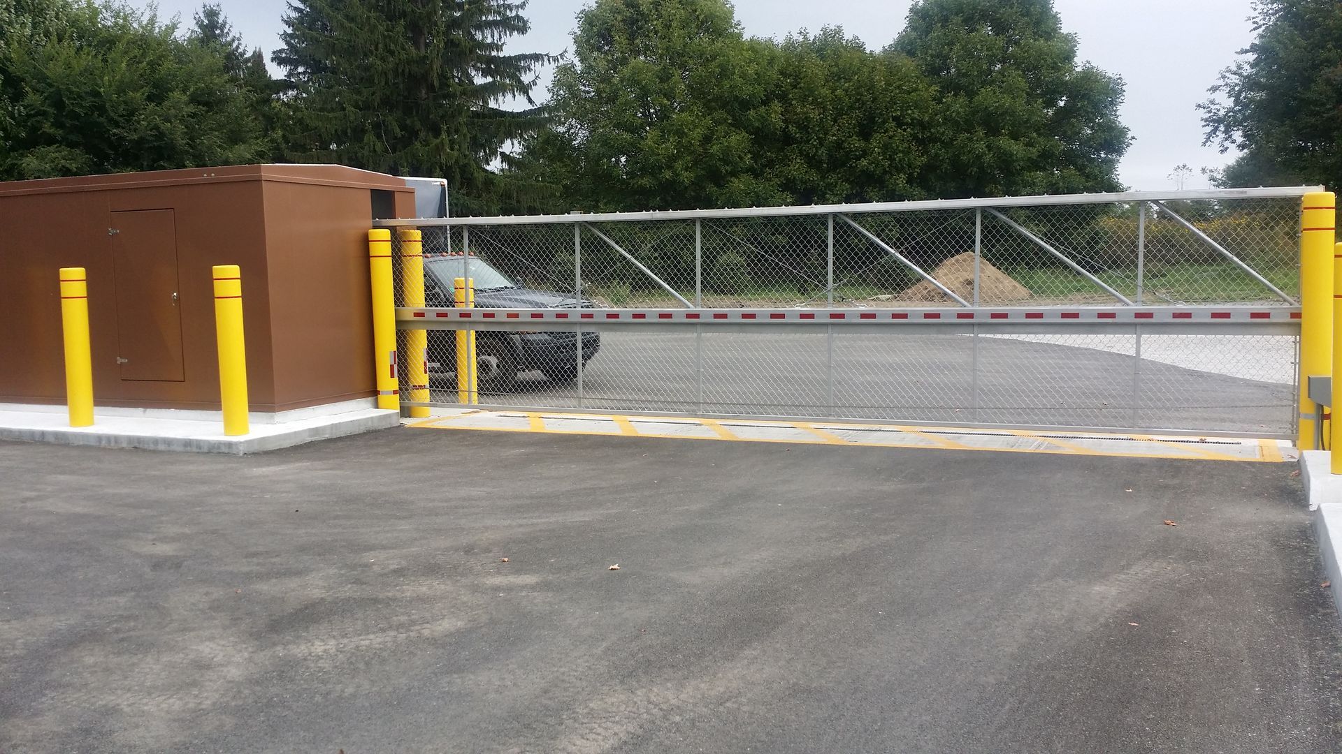 Un parking avec un portail coulissant et des poteaux jaunes.