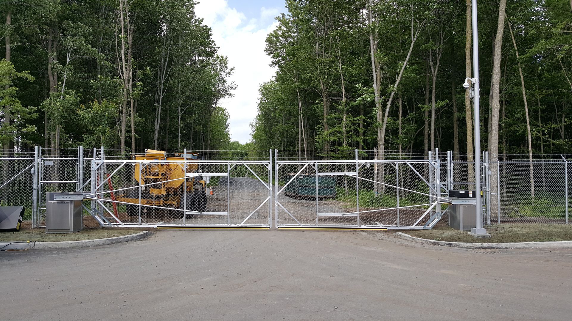 Une zone clôturée avec un portail et des arbres en arrière-plan.