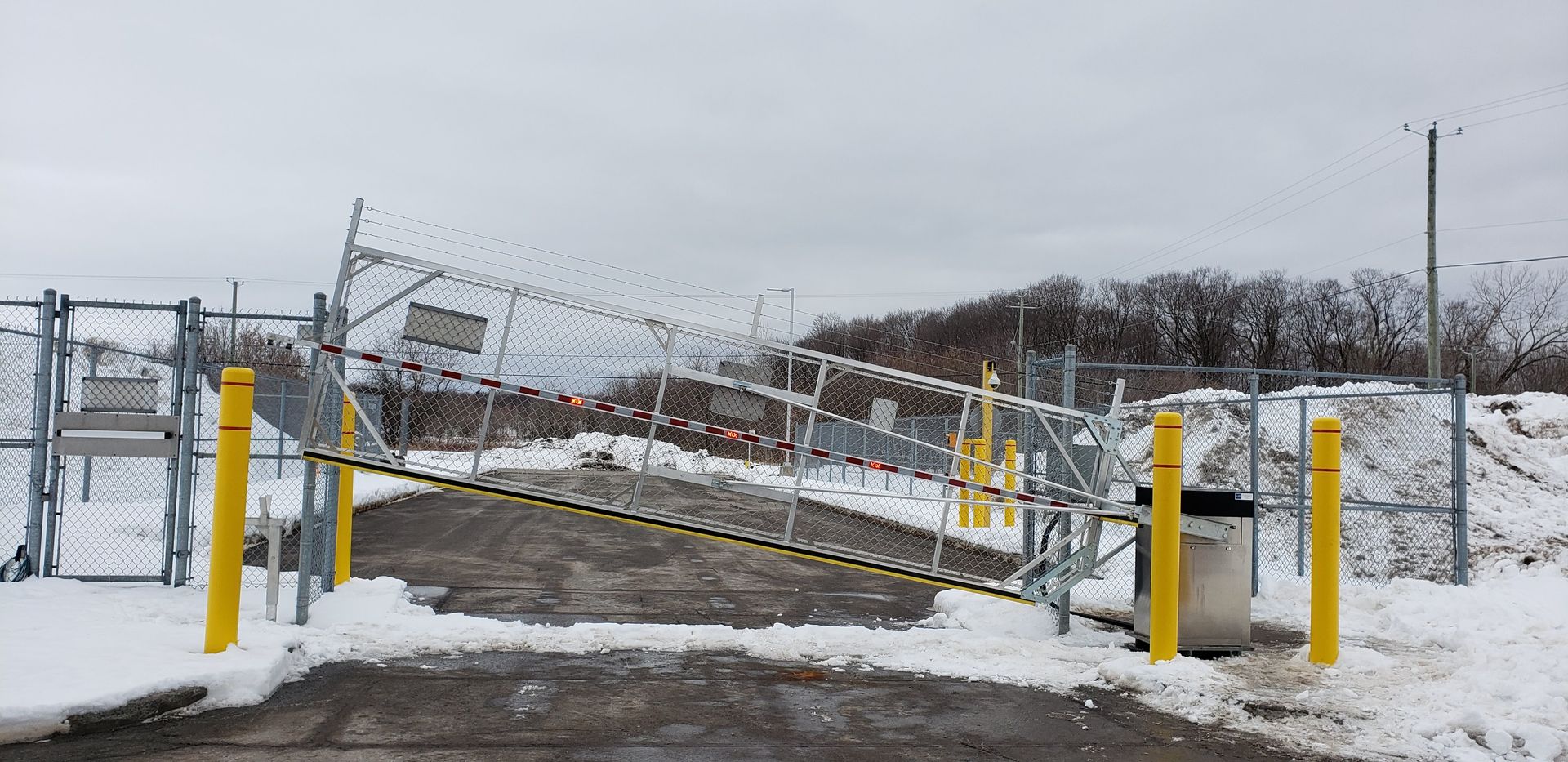 Un parking enneigé avec une clôture et une poubelle.