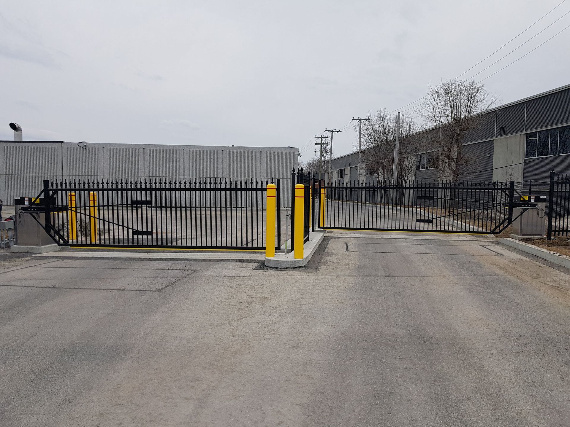 Une clôture noire et jaune entoure un parking devant un grand bâtiment.