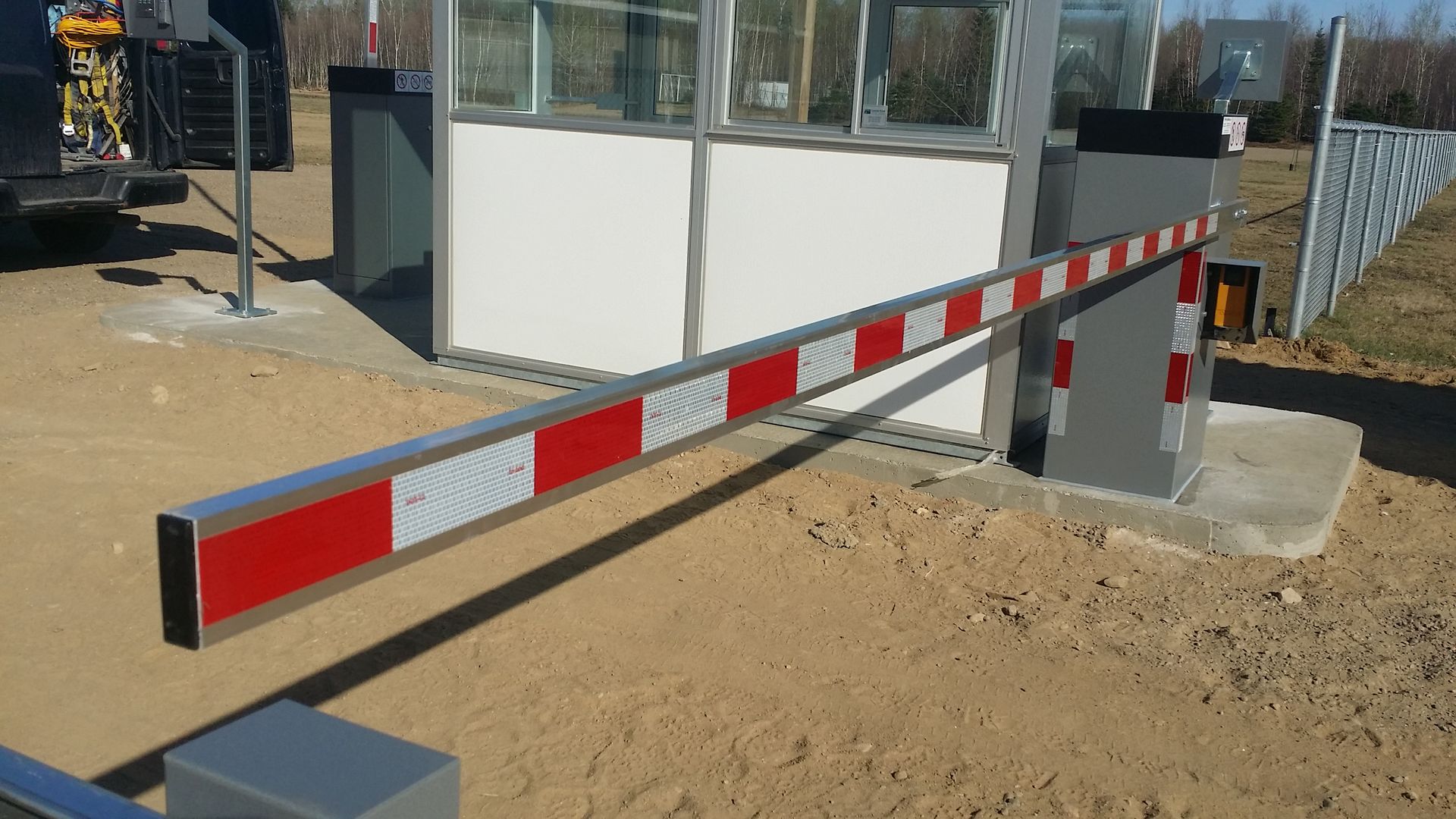 Une barrière rouge et blanche est posée dans la terre devant un bâtiment.