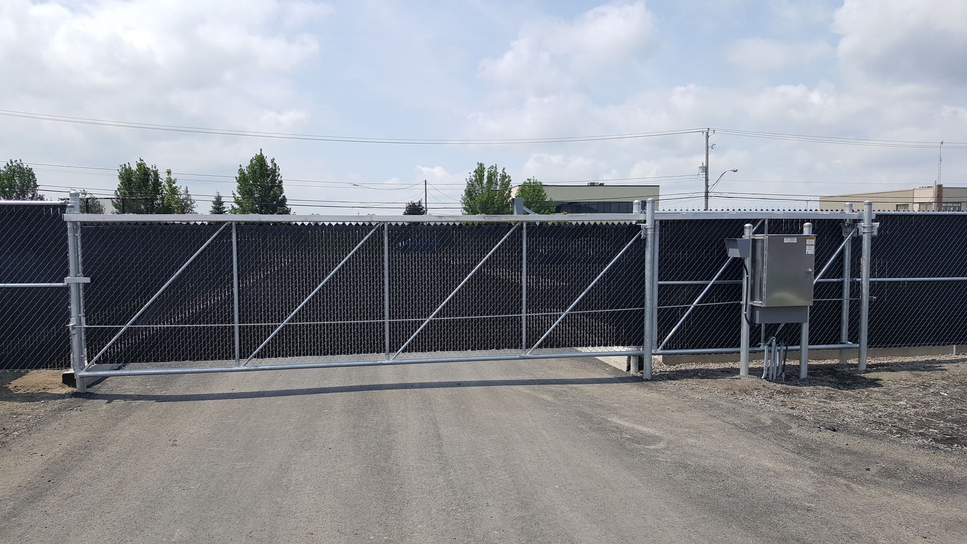 Un portail coulissant se trouve sur le côté d'un chemin de gravier à côté d'une clôture à mailles losangées.