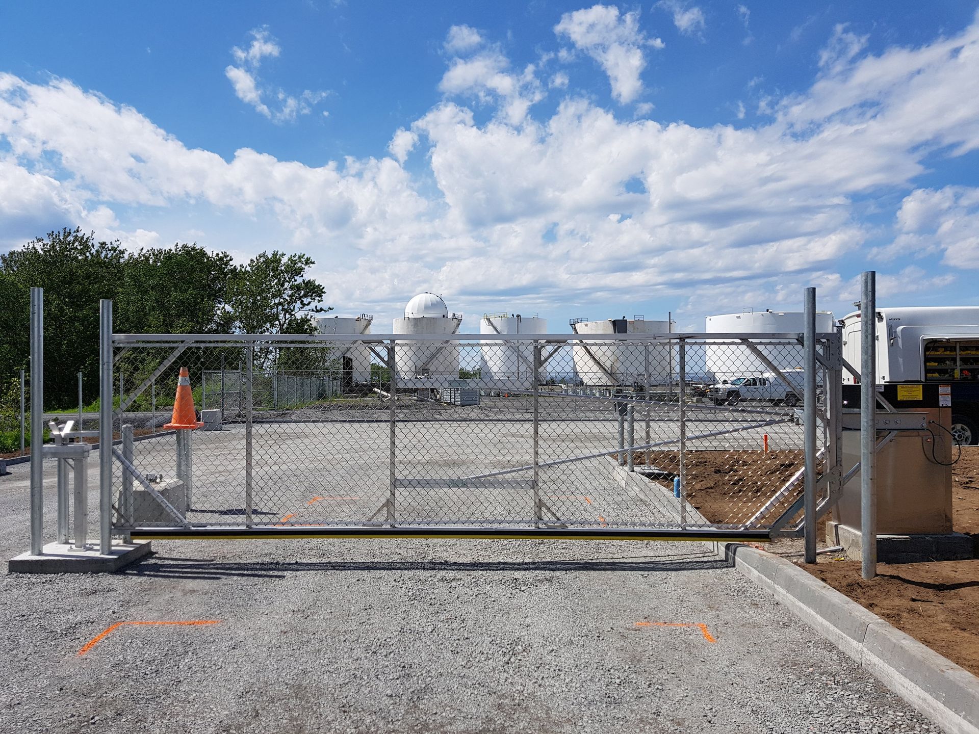 Une clôture à mailles losangées entoure un chantier de construction avec de nombreux chars en arrière-plan.