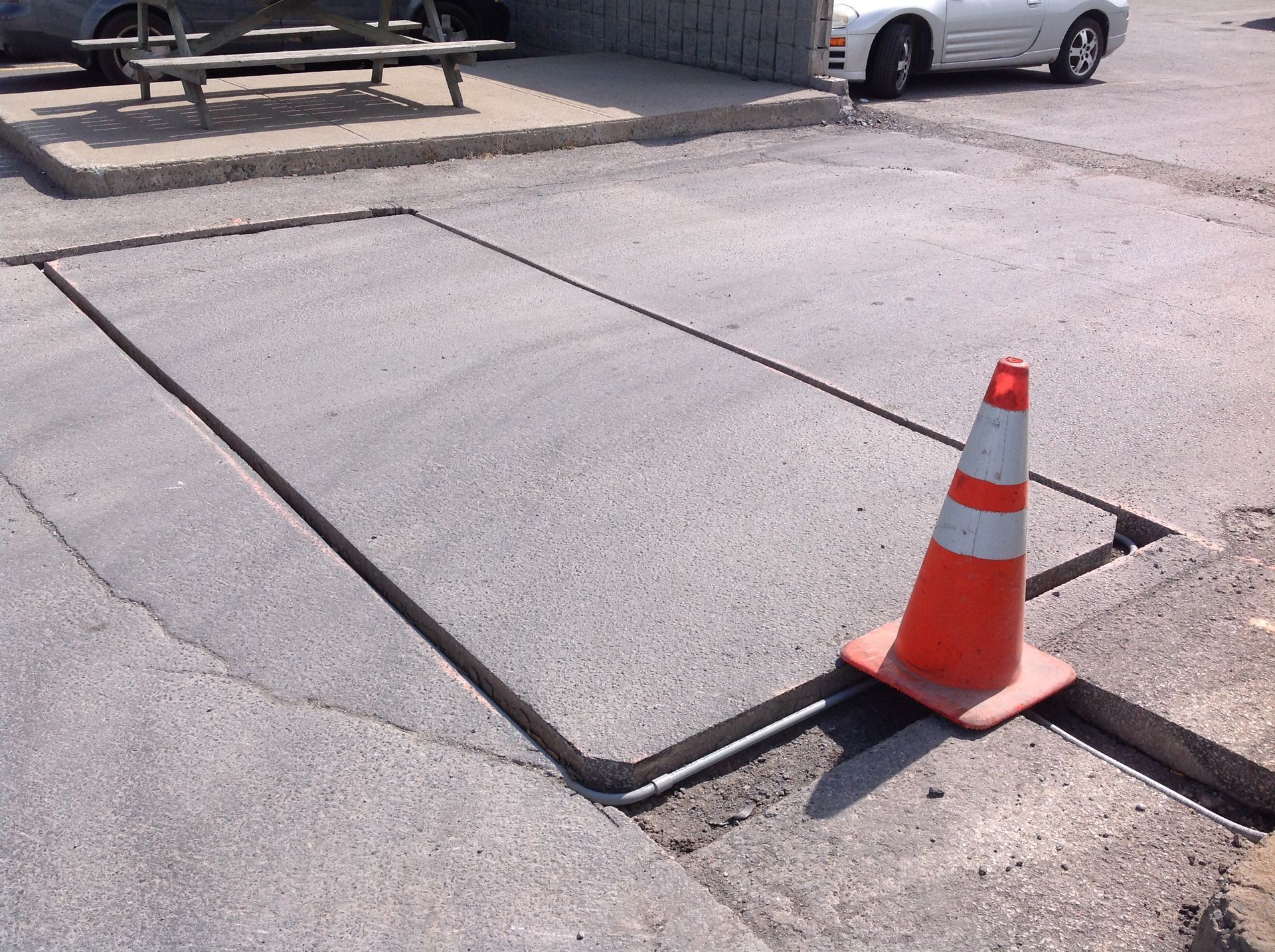 A white car is parked in a parking lot next to a cone