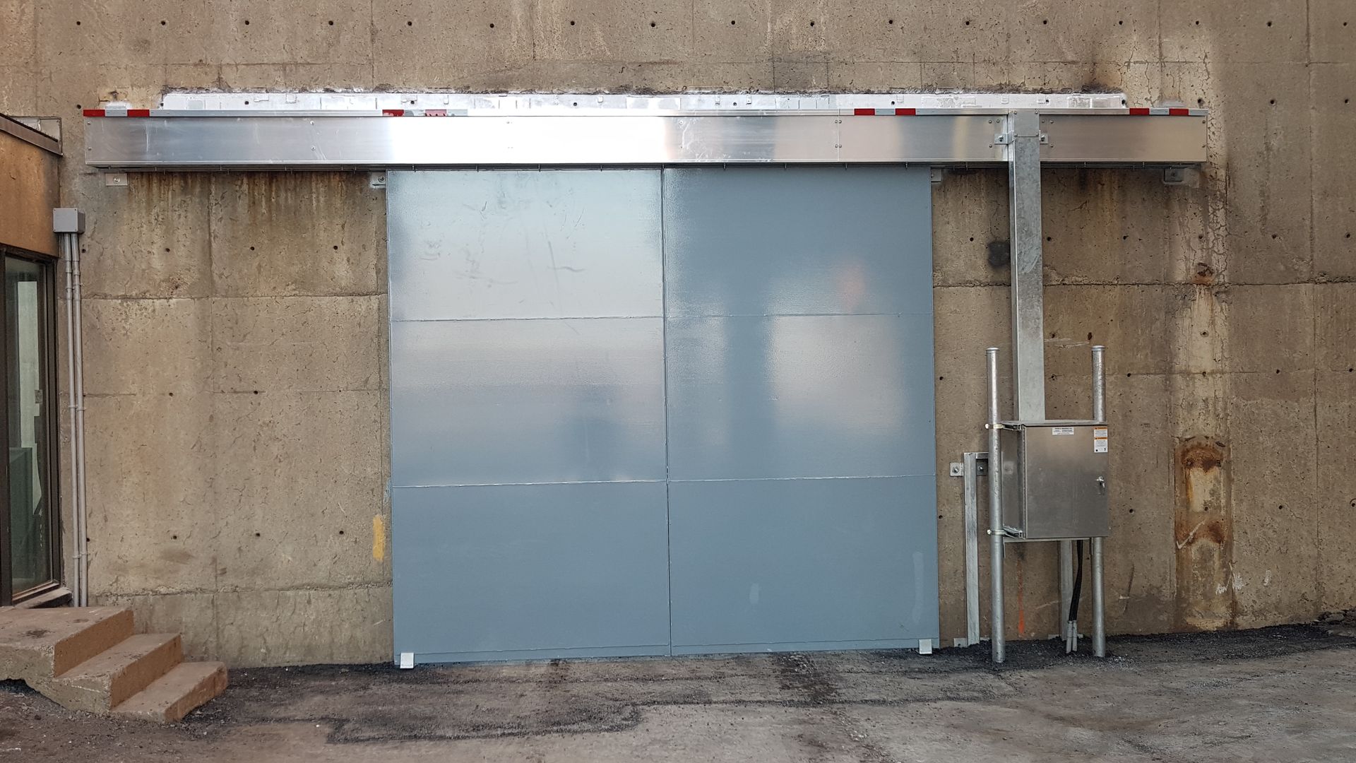 Une grande porte coulissante est fixée à un mur en béton.