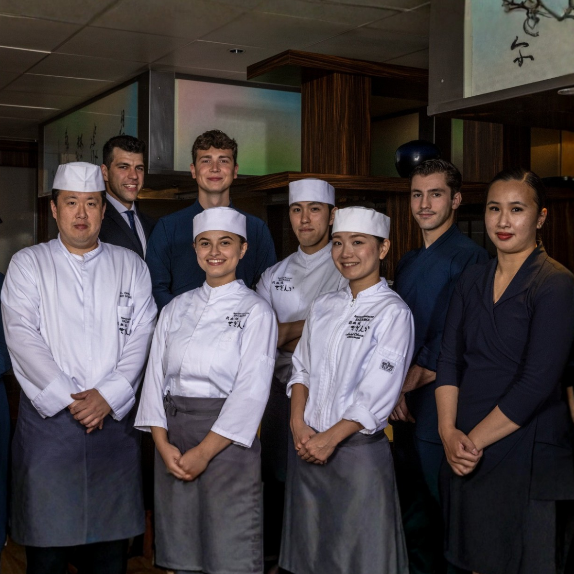 Restaurant staff group photo. Several people in chef whites and formal attire stand together indoors.