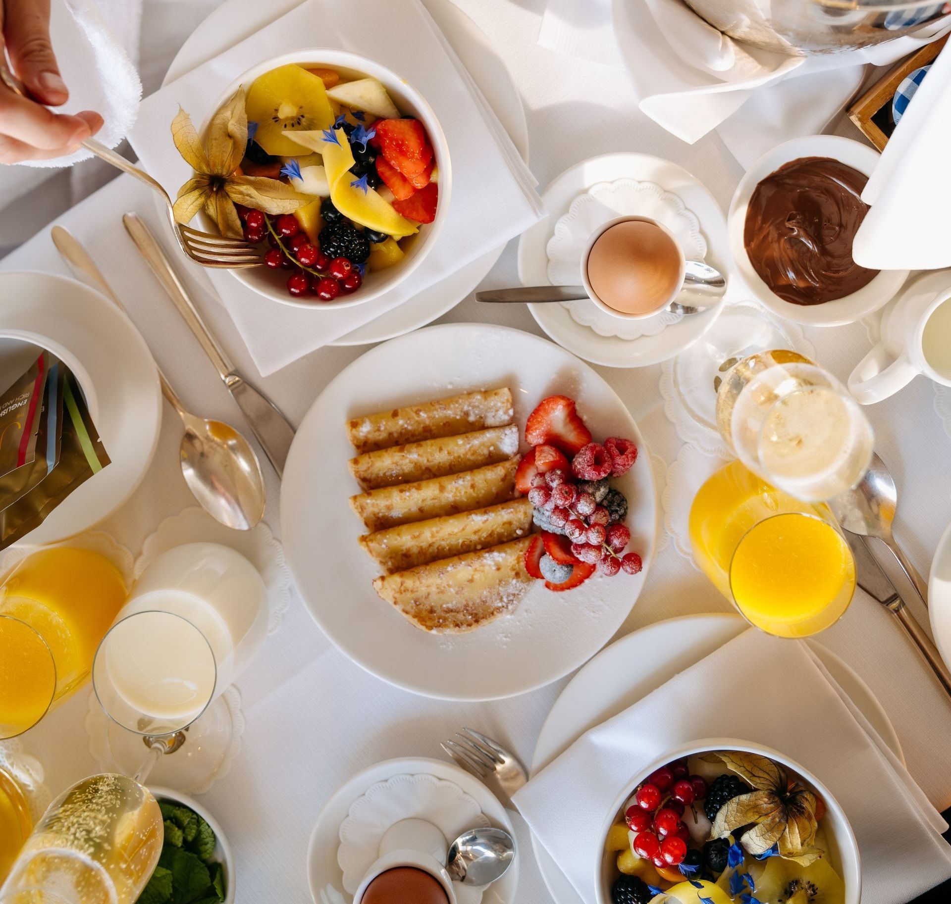 Breakfast table with fruit, toast, eggs, orange juice, and chocolate spread.
