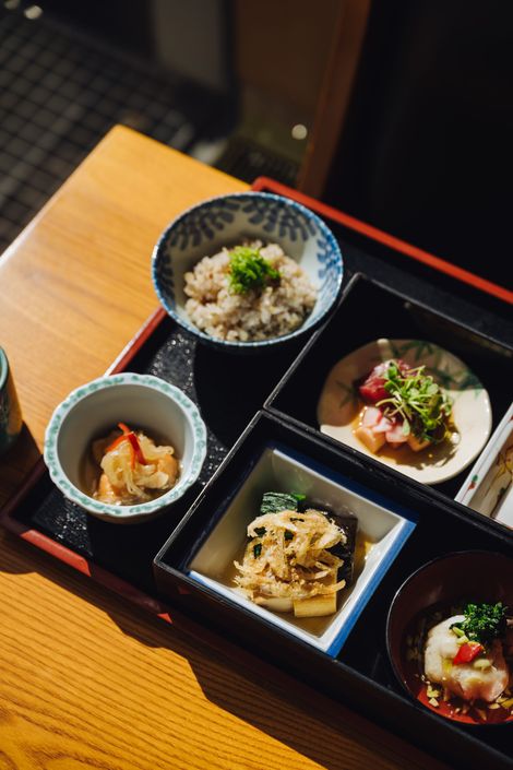 Bento box with various Japanese dishes, including sushi, seafood, and salad, presented on a dark surface.