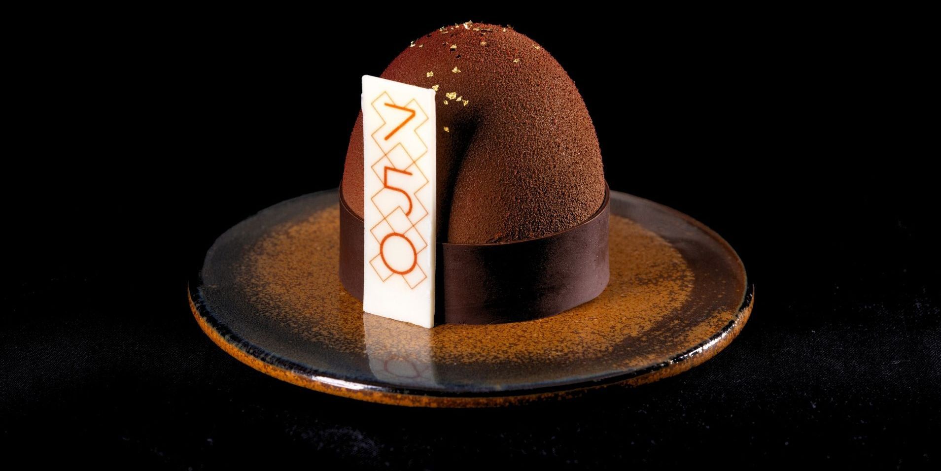 Chocolate dessert on a plate, with a tag that says "150". Dark background.