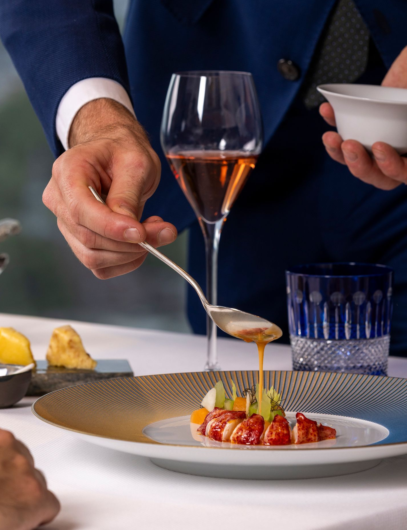 Server pours sauce onto a plate of food. Formal setting with cityscape background.
