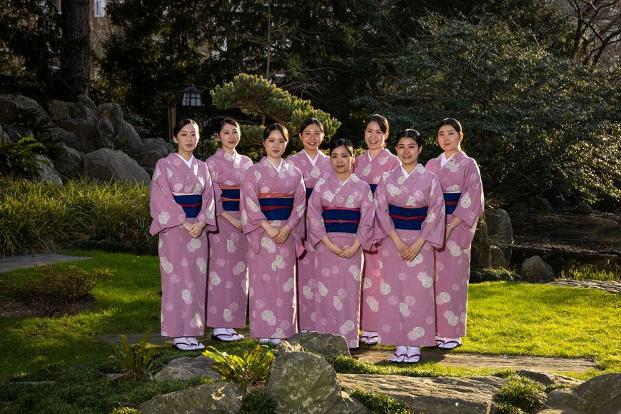 Two women in yukata stand in front of a green, leafy background.