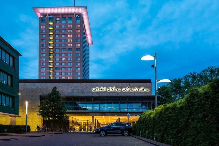 Hotel with tall tower, illuminated sign and entrance, blue car parked out front.