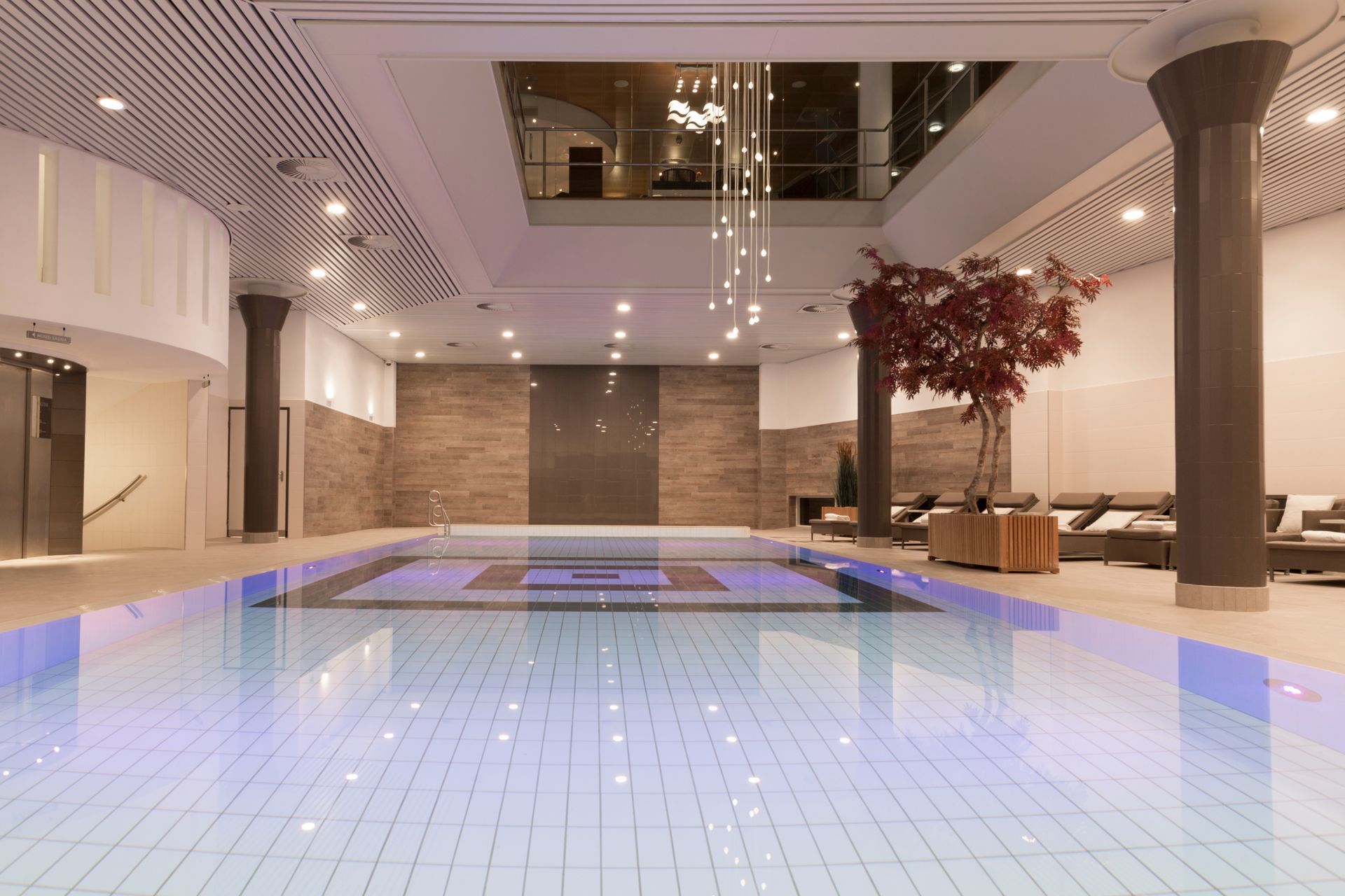 Indoor swimming pool with decorative tile, columns, and seating area.