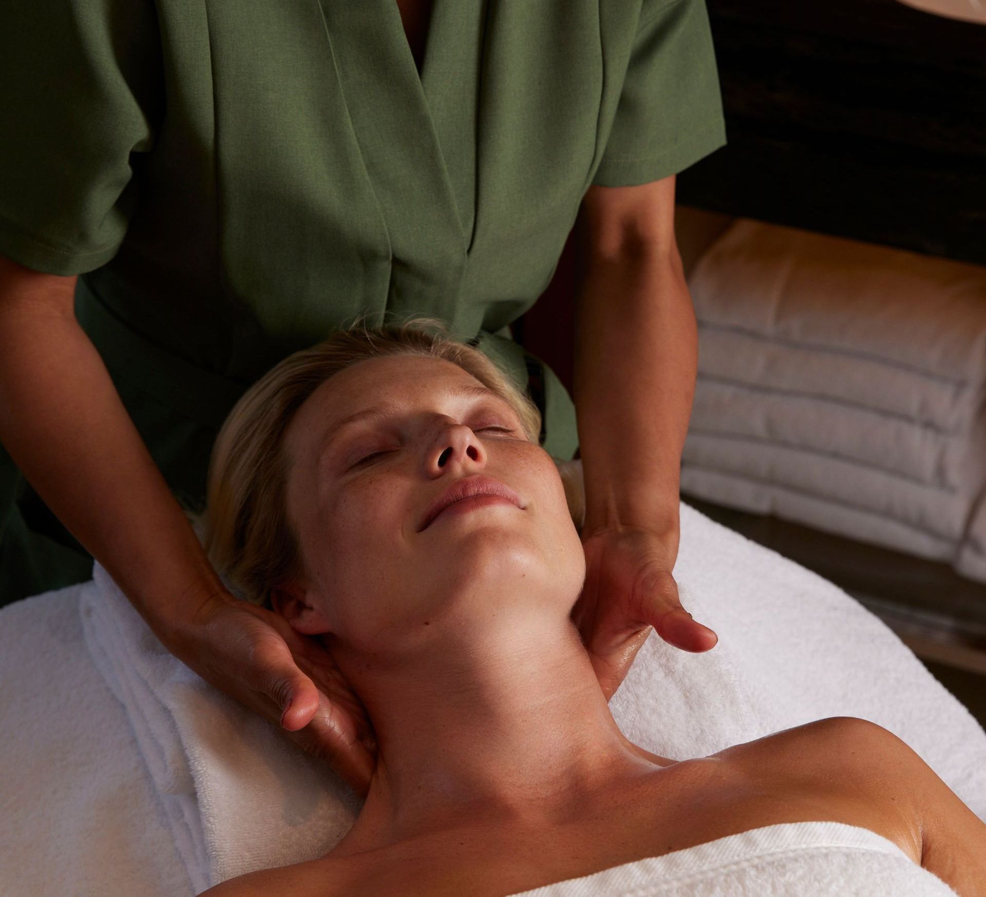 Person receiving neck massage in spa setting. Hands on neck, eyes closed, white towel.