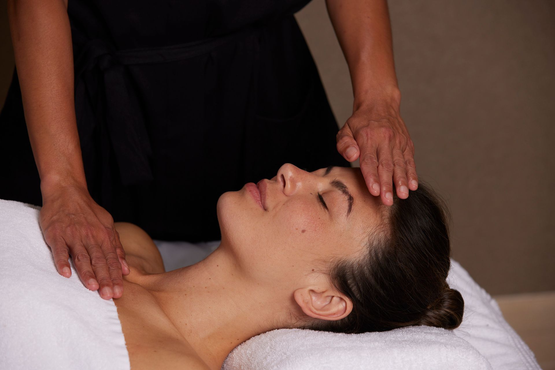 Person receiving a facial massage at a spa; hands on forehead and neck.