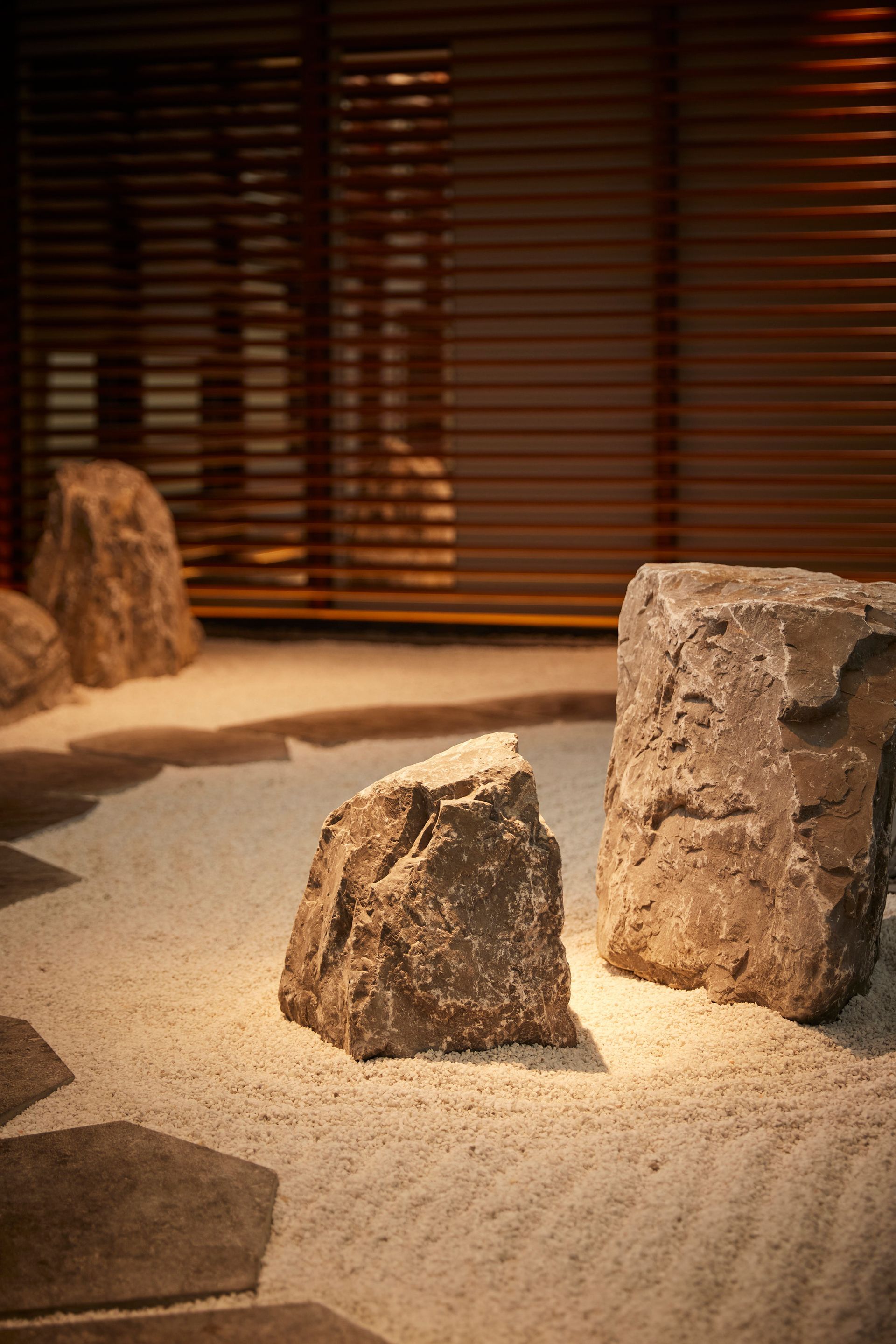 Zen garden with large stones in sand, wooden screen background, warm light.